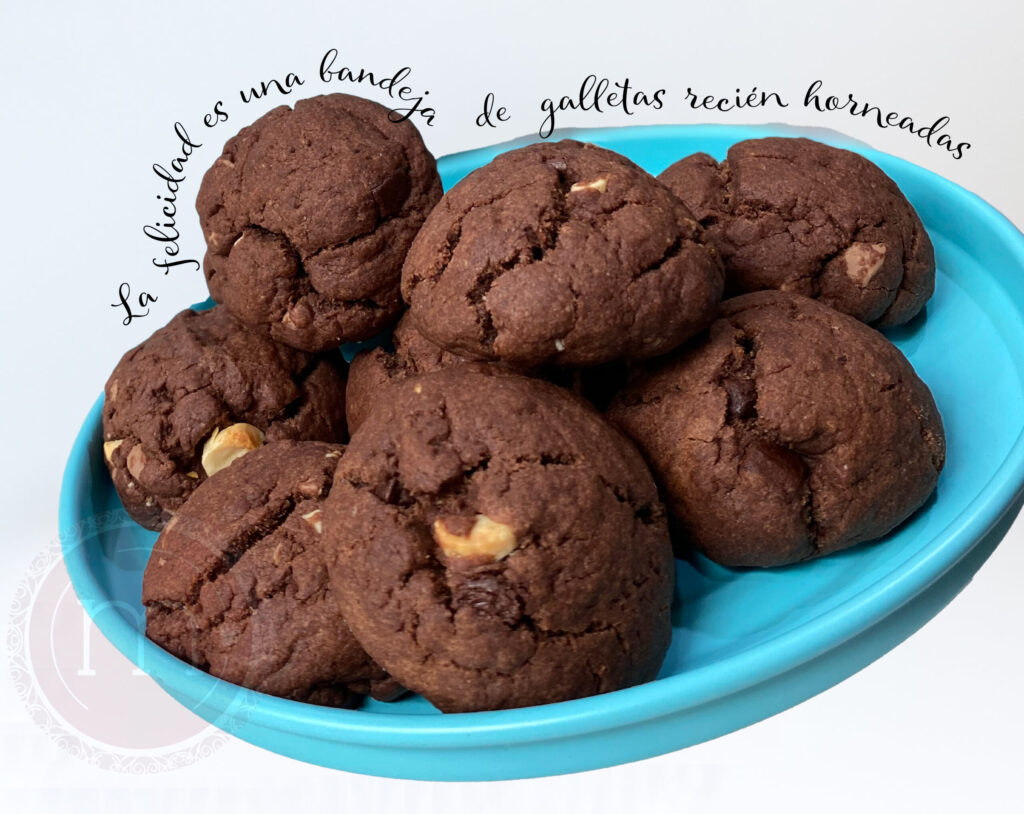 Un grupo de galletas con chispas de chocolate y trozos de nuez. Sobre la imagen de las galletas se coloca un texto que dice "La felicidad es una bandeja de galletas recién horneadas".