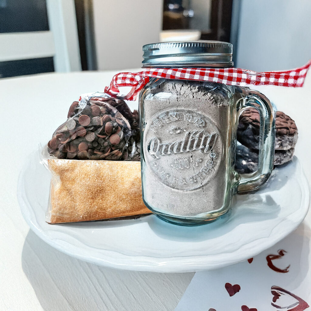 Un mason jar relleno con harina, detras de él se coloca una bolsa con azúcar y una bolsa con chispas de chocolate. Todo el kit se coloca sobre una base blanca. Este kit es ideaal para hornear el día del padre para pasar un rato de calidad.