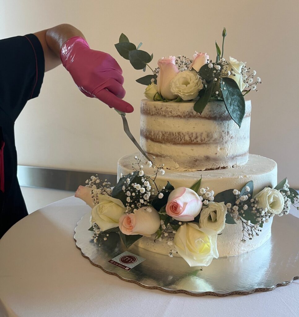Una persona está decorando un pastel. Los diseños de pasteles para bodas con flores se colocan al momento para garantizar la calidad y se colocan cuidado. Este pastel es de dos pisos y tiene grandes flores rosas.