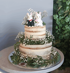 Un pastel de boda de dos pisos decorado con flores naturales. En la parte superior se coloca una pareja de conejos que representa una pareja de novios. Los pasteles caseros puebla de m de motivos como este son personalizados