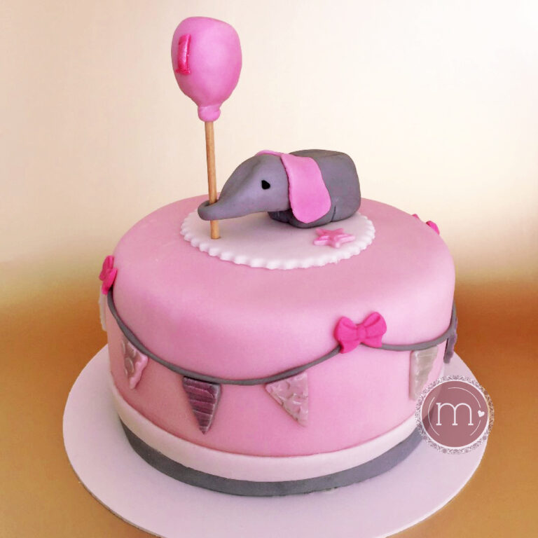 Un mini pastel personalizados con una decoración de fondant en color rosa. En la parte superior se coloca una figura de elefante hecha de fondant y a su vez sostiene un globo de fondant. El pastel es ideal para una sesión de fotos smash cake. El pastel se coloca sobre una base de color blanco.