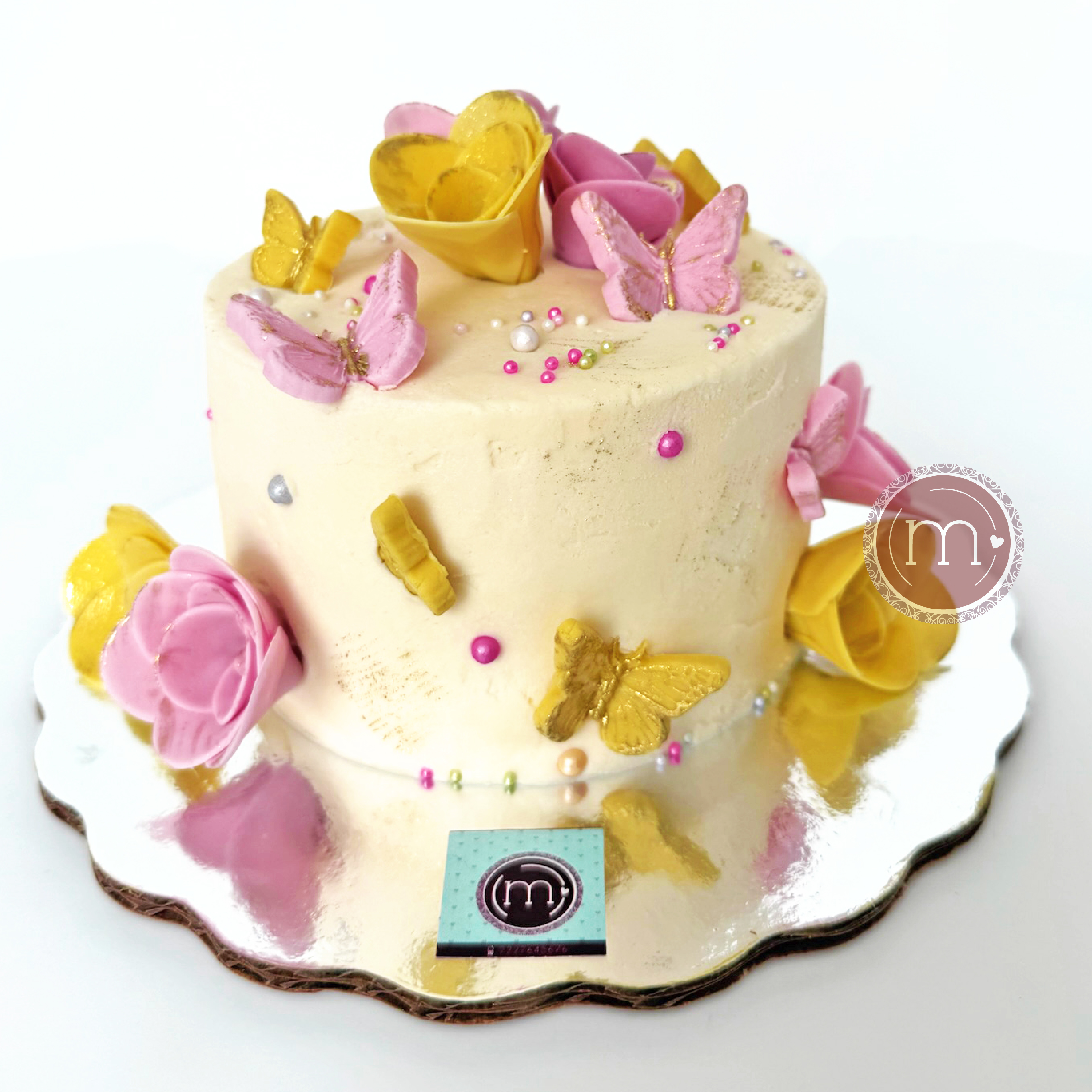 Un mini pastel personalizado con mariposas y flores de fondant de colores blanco y amarillo. El pastel es de color blanco y se coloca sobre una base reflectante. Estos mini pasteles son ideales para una sesión de fotos smash cake.