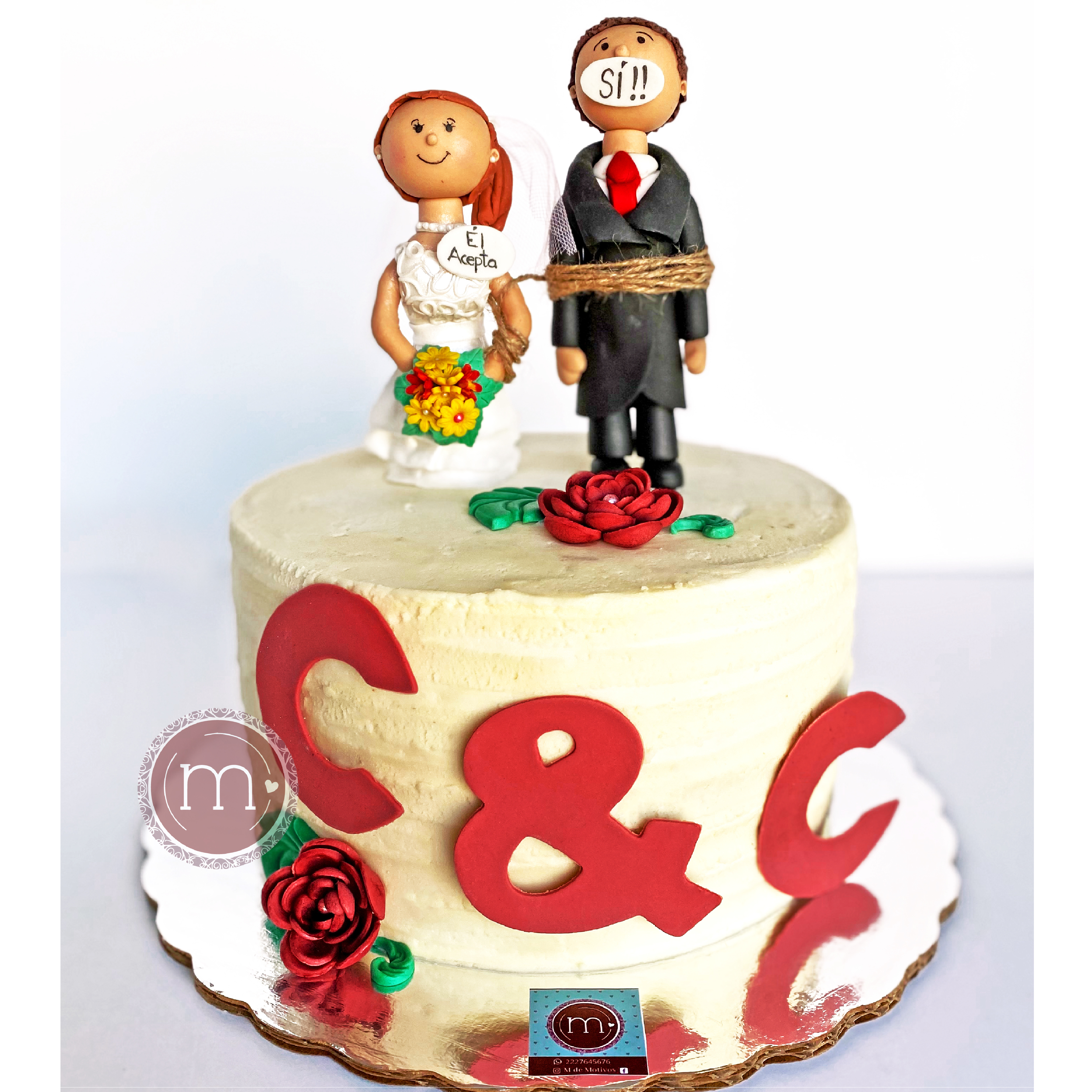 Un pastel decorado con dos personajes vestidos de "novia" y "novio", A su vez hay decoraciones de flores de fondant y en la parte frontal del pastel hay dos letras "C" y una "&" de fondant de color rojo. El pastel se coloca sobre una base de color plateado. Este pastel de bodas está decorado con figuras de novios de fondant.