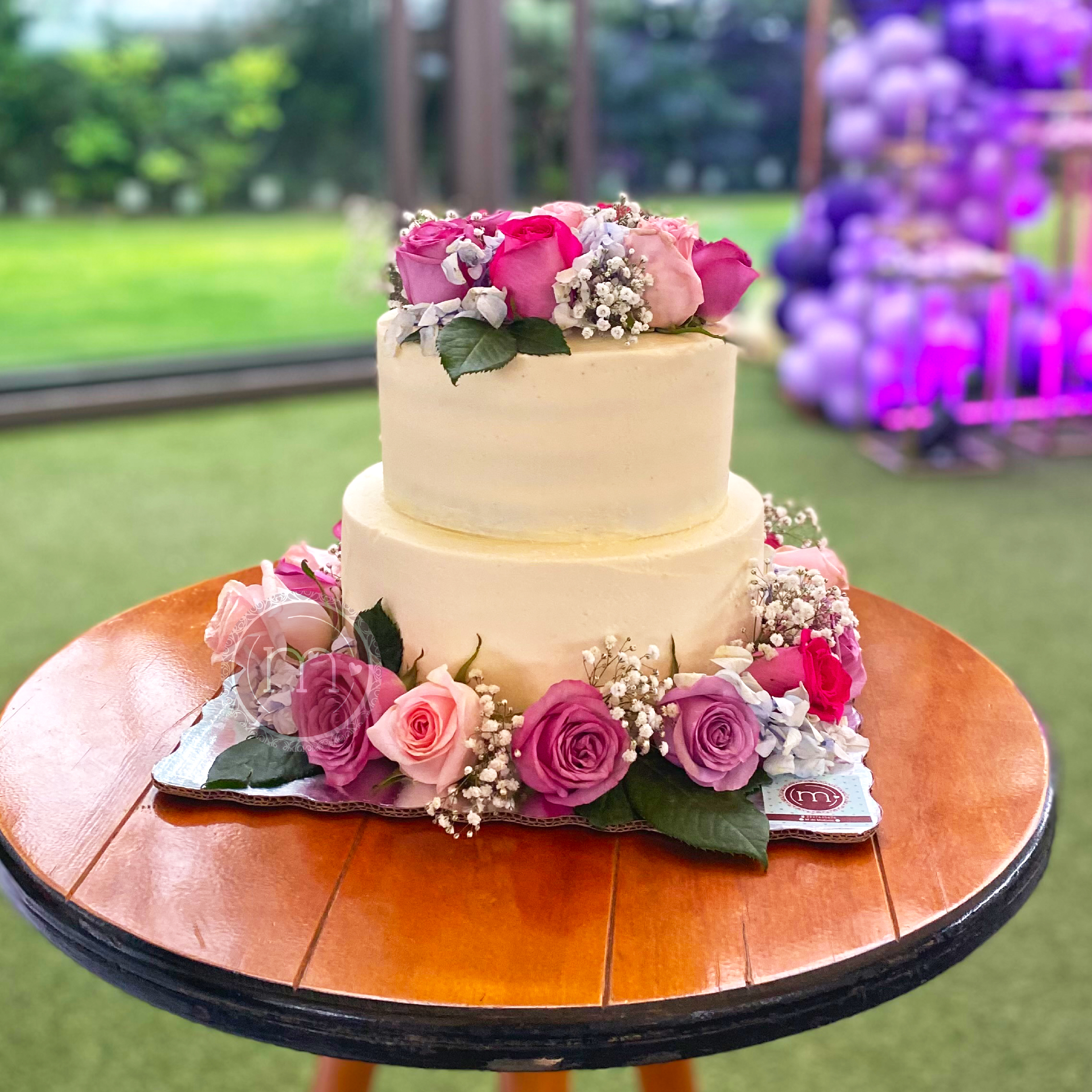 Un pastel de boda de dos pisos decorado con flores naturales. Los pasteles caseros de "m de motivos" son talmente personalizados. El pastel se coloca sobre una mesa de madera.