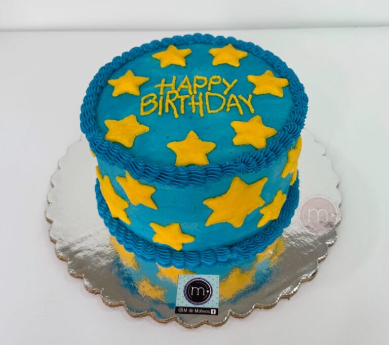 Este pastel personalizado tiene una decoración de betún color azul con estrellas amarillas. En la parte superior del pastel se escribe "Happy Birthday". El pastel se coloca sobre una base reflectante.