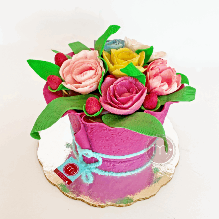 Los pasteles fondant como este, para cumpleaños decorado con detalladas flores de crema de mantequilla en tonos rosa, amarillo y fucsia. Entre las flores se encuentran hojas verdes y fresas rojas. El pastel está adornado con un lazo de fondant azul y descansa sobre una base de lámina dorada.