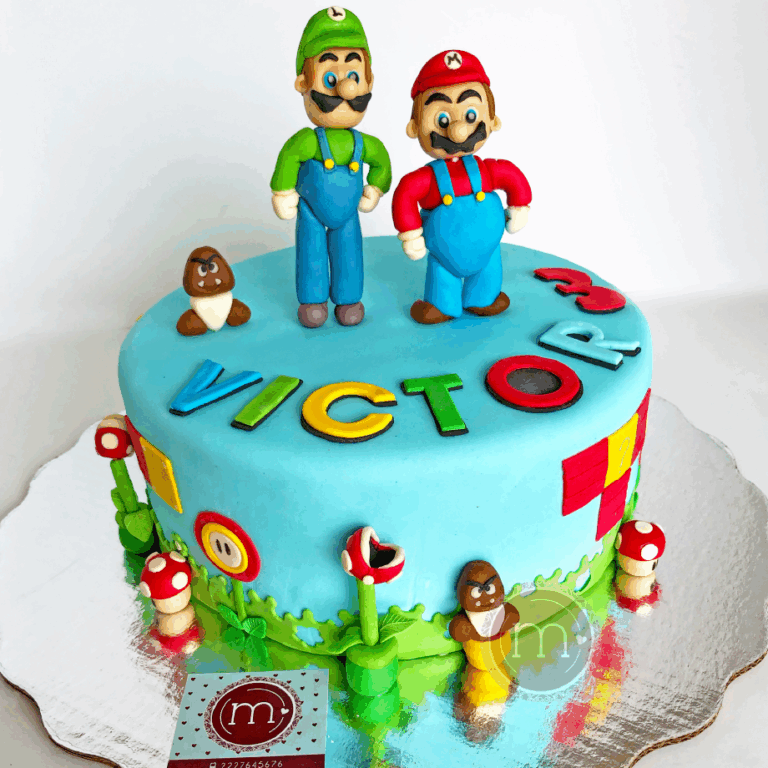 Un colorido pastel de cumpleaños de Mario Bross presenta una base de glaseado azul con decoraciones de fondant de Mario, Luigi, hongos y monedas de la serie Super Mario. El nombre "Víctor" está escrito en letras multicolores en la parte superior. El pastel se asienta sobre una base plateada reflectante. Este tipo de decoraciones coloridas lucen bastante bien en los pasteles fondant