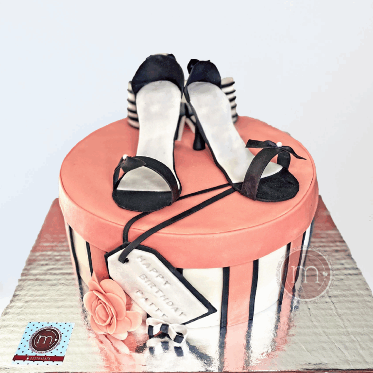 Un pastel de fondant en forma de caja circular con franjas rosas, negras y blancas. Encima tiene un par de zapatillas color negro, igualmente de fondant. En la parte frontal de la caja se ve una etiqueta de color blanco y dice "HAPPY BIRTHDAY PATTY", junto a esta pieza hay una flor y un moño pequeño, hechos de fondant. Los pasteles fondant son muy atractivos para muchas personas. El pastel se coloca sobre una base rectangular color plateado reflejante.