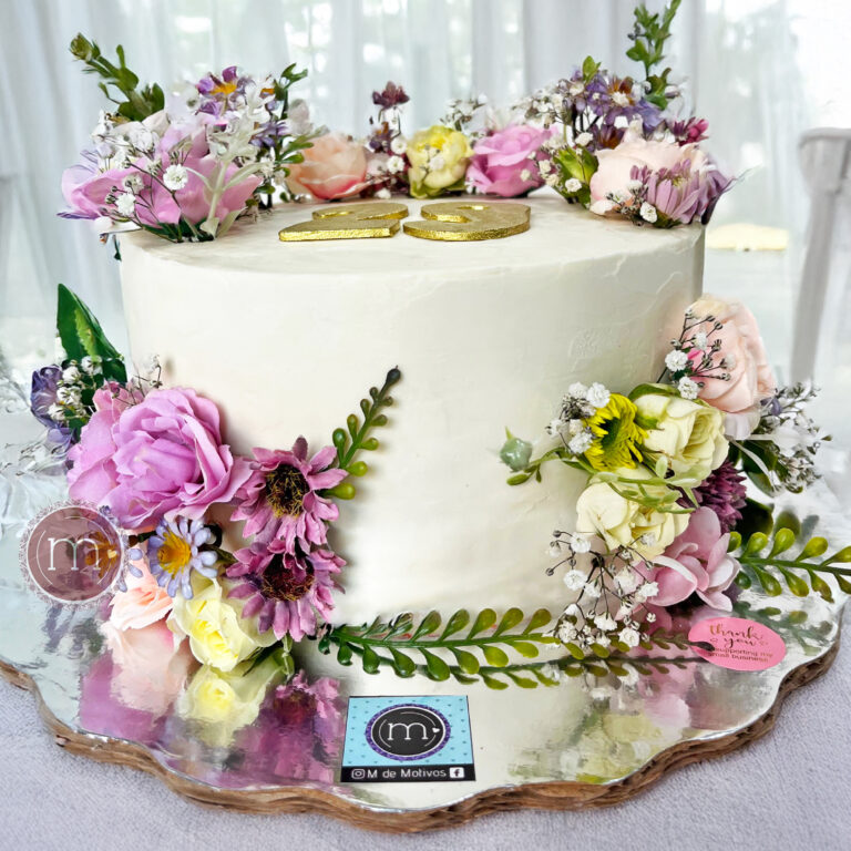 Un pastel blanco decorado con flores natuarales de tonos morados y verdes. En la parte superior se colca el número "29" hecho con fondant. Las flores para pasteles personalizados son seleccionadas cuidadosamente. El pastel se coloca sobre una base reflectante.