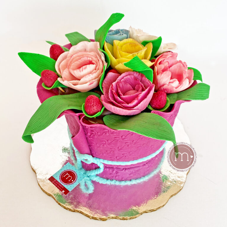 Un pastel en forma de ramo de flores hecho con fondant. Las flores tienen forma de rosa y son de colores variados. En la repostería "m de motivos" se hacen pasteles personalizados con fondant. El pastel se coloca sobre una base reflectante.