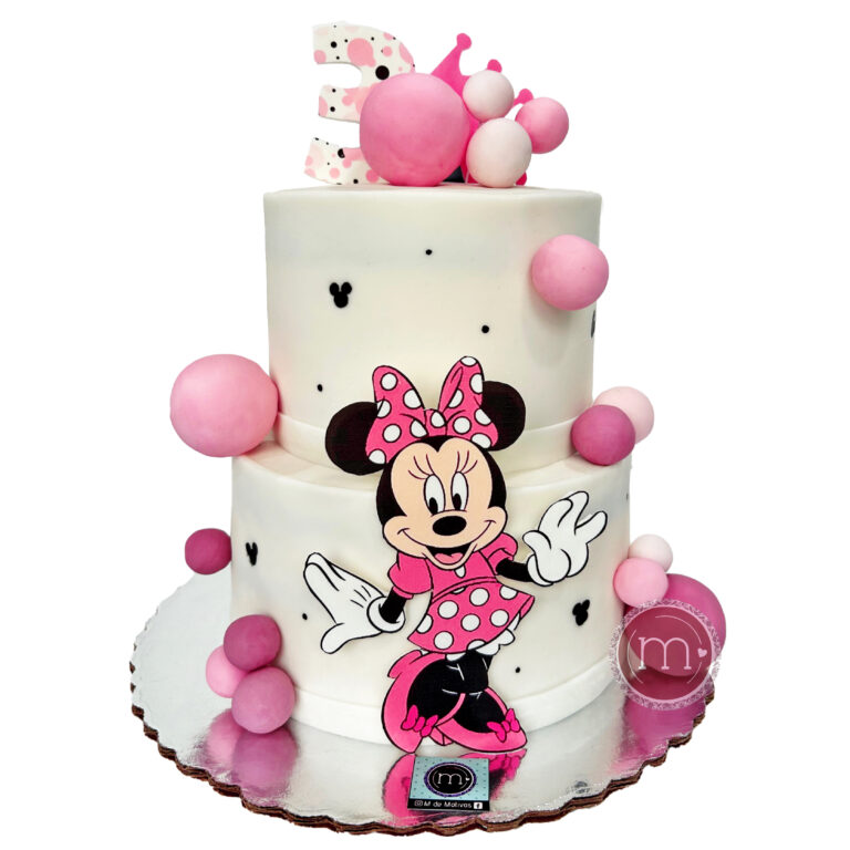 Un pastel de dos pisos de color blanco tiene decoraciones con temática del personaje "Minnie" En la repostería "M de motivos" se hacen pasteles personalizados con temáticas. El pastel se coloca sobre una base reflectante.