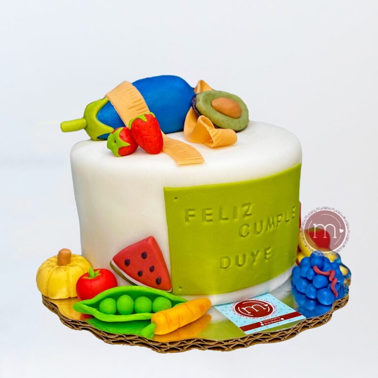 En repostería "m de motivos" realizamos pasteles personalizados como este, que está decorado con fondant creando elementos como frutas y verduras cumpliendo con una temáticca alimenticia. El pastel, como se lee en la placa de la parte frontal, está elaborado para celebrar a una nutriologa. El pastel se coloca sobre una base reflectante.