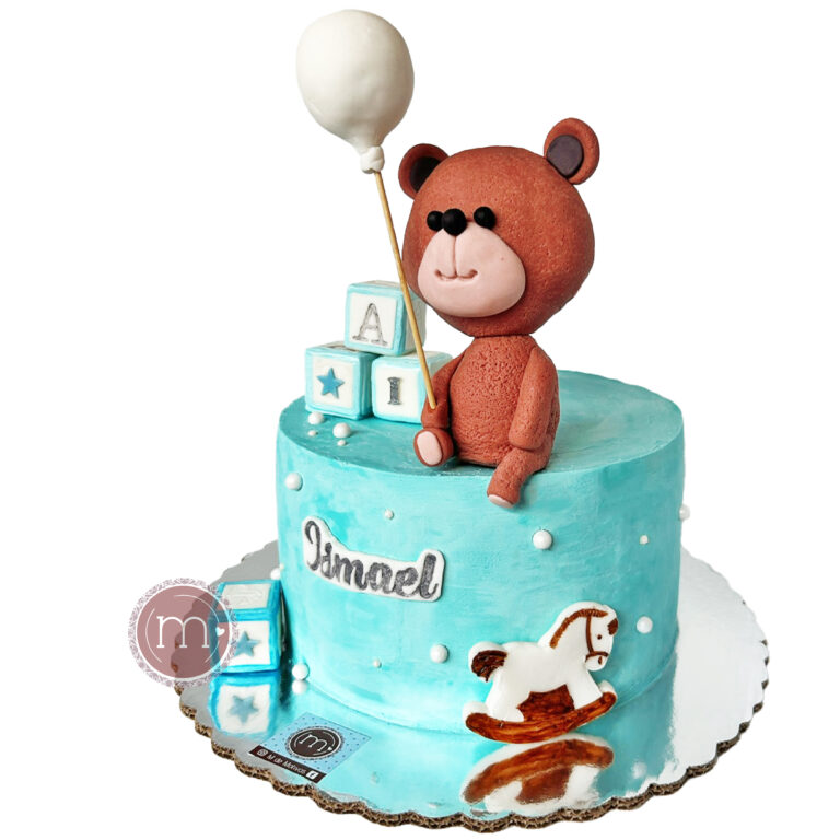Pasteles caseros decorados para sesión de fotos smash cake de bebés, como este, que está decorado con un betún azul y con figuras hechas de fondant, como unos dados y un oso cafe que se colca sobre el pastel.