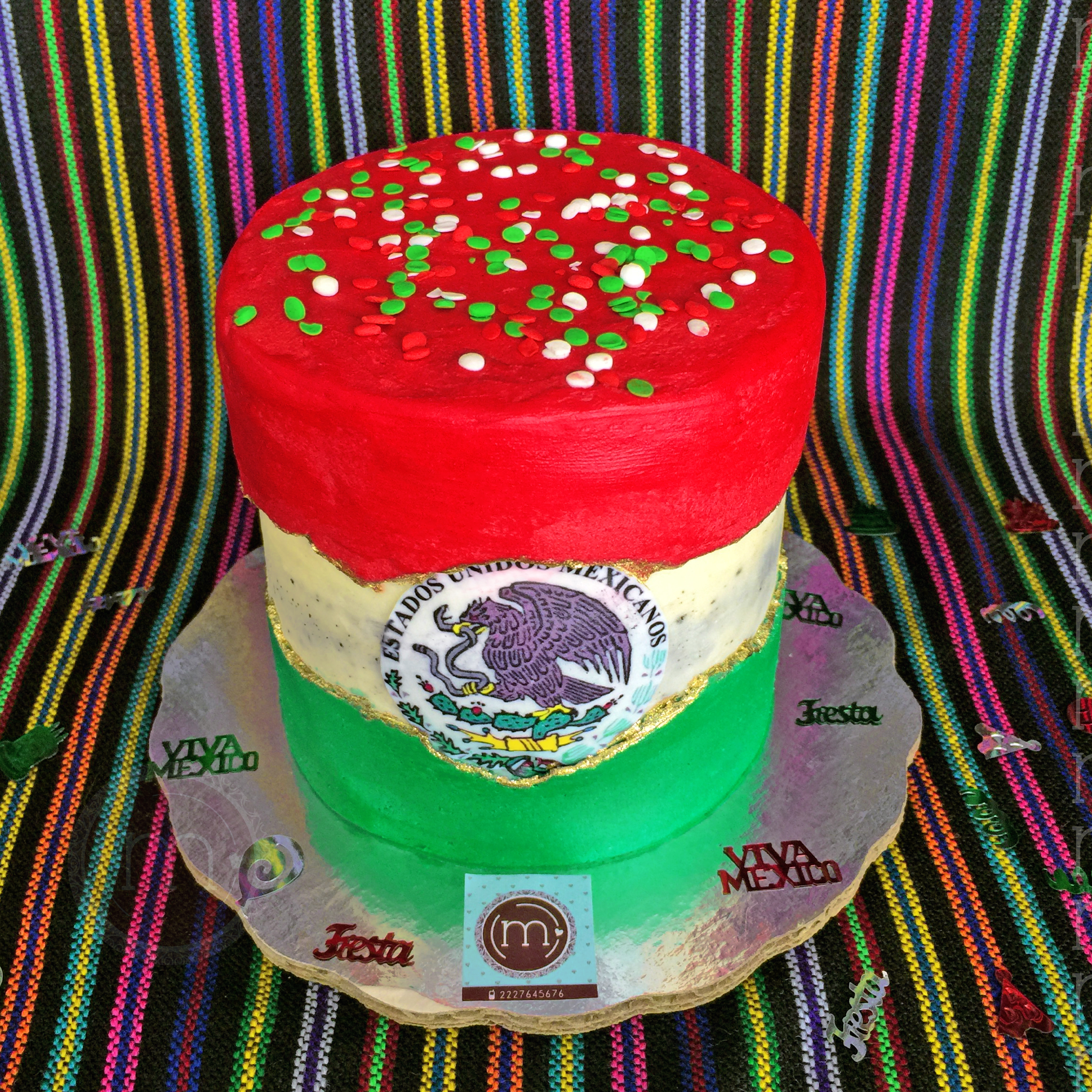 "Pastel tricolor para noche mexicana. Se ve el pastel cortado por un rebana, el pan es de chocolate. El pastel se coloca sobre una base reflectante y un mantel de colores.