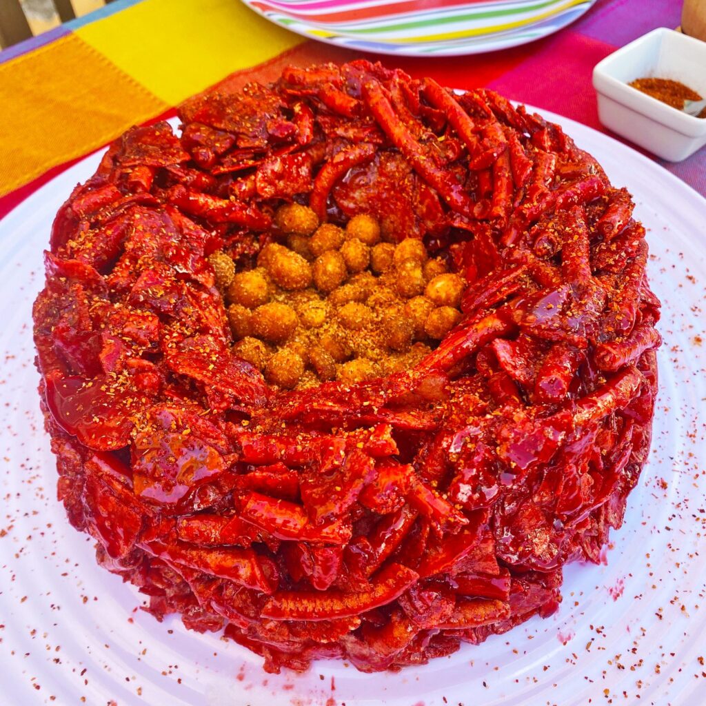 Botana para noche mexicana. Rosca de chamoy hecha con frituras picantes con un centro de cacahuates. La rosca se coloca sobre un plato blanco.