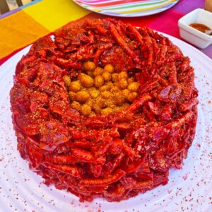 Botana para noche mexicana. Rosca de chamoy hecha con frituras picantes con un centro de cacahuates. La rosca se coloca sobre un plato blanco.