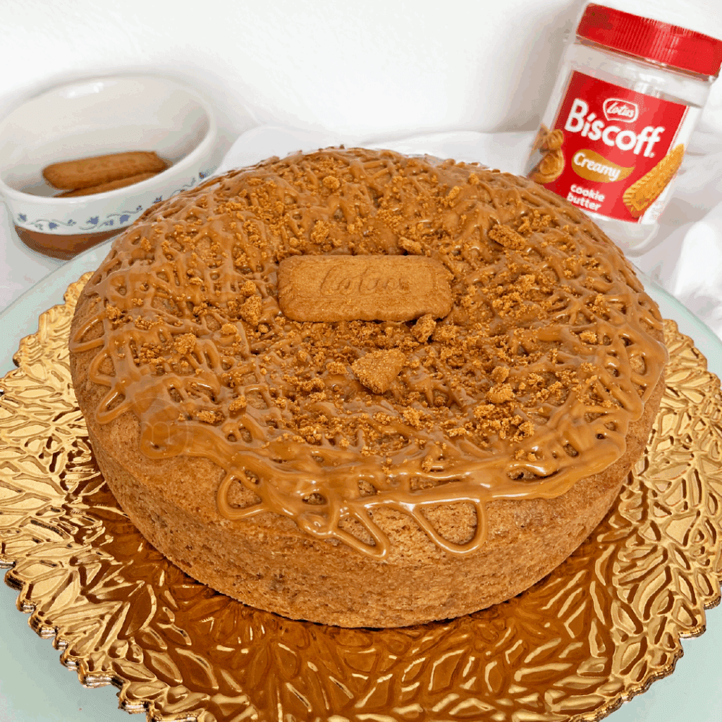 Un pastel de galleta Lotus cubierto con una reja de crema biscoff y u una galleta Lotus encima. Pasteles y postres de otoño crujientes en m de motivos. El pastel se coloca sobre una base dorada, detrás hay un envase de Bisoff y un recipiente con galletas Lotus.