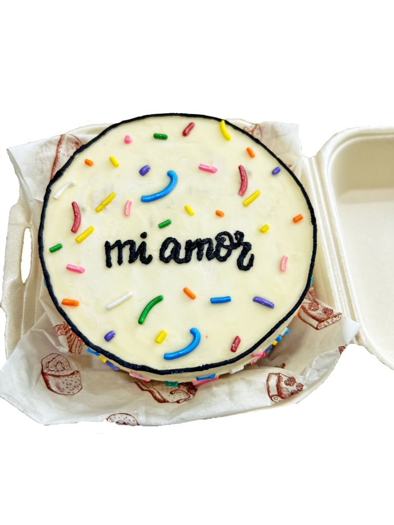 Un mini pastel decorado con betún blanco y sprinkles de colores. El pastel tiene escrito "mi amor". Estas ideas para san valentin de pasteles con diseños personalizados son populares.
