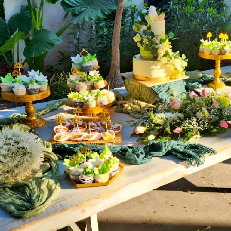 Una mesa de postres con cupcakes y un pastel decorados con temática de "La Princesa y el Sapo". Además de pasteles de boda, las mesas de postres son parte esencial de una boda.