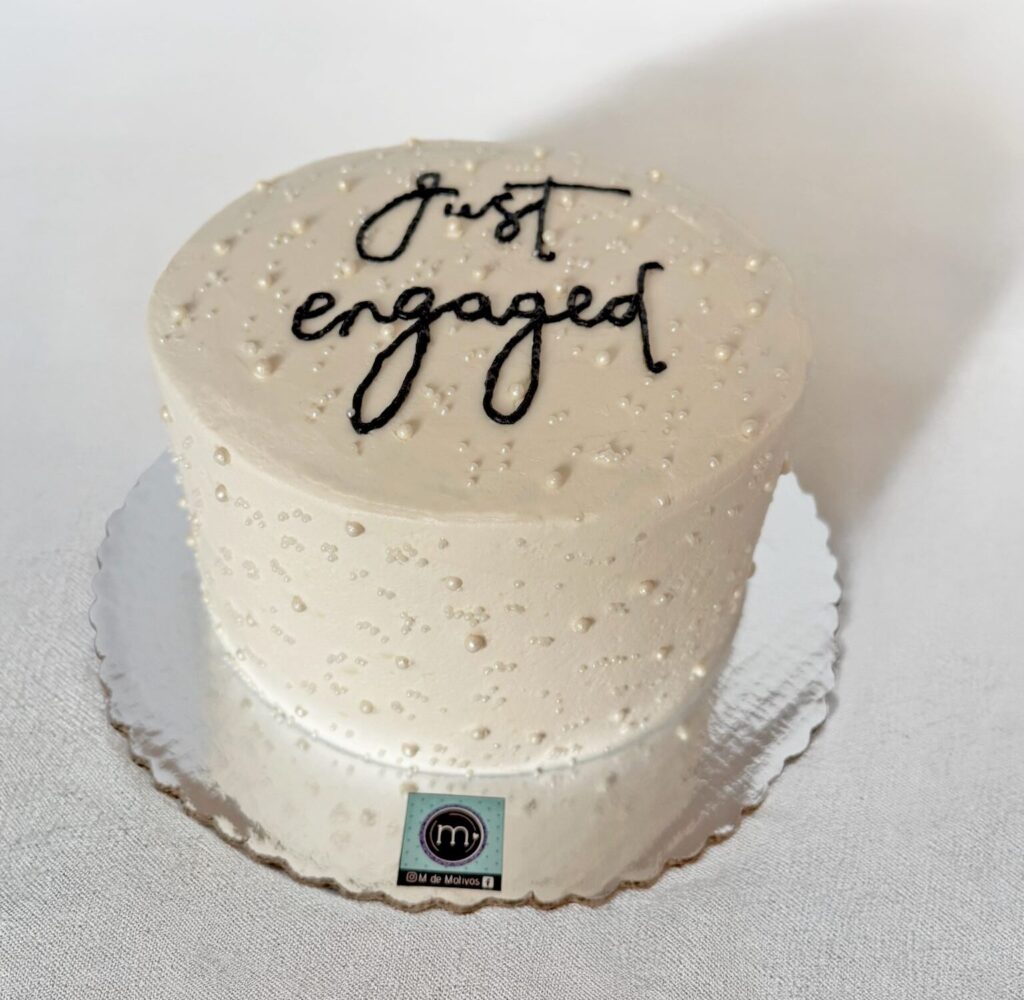 Un pastel de boda decorado con perlas con el texto "Just Engaged". En m de motivos, repostería de Puebla, ofrecemos pasteles de boda sencillos personalizados. El pastel se coloca sobre un mantel de tela color blanco.