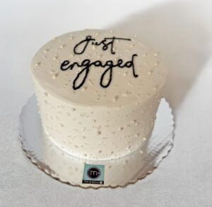 Un pastel de boda decorado con perlas con el texto "Just Engaged". En m de motivos, repostería de Puebla, ofrecemos pasteles de boda sencillos personalizados. El pastel se coloca sobre un mantel de tela color blanco.