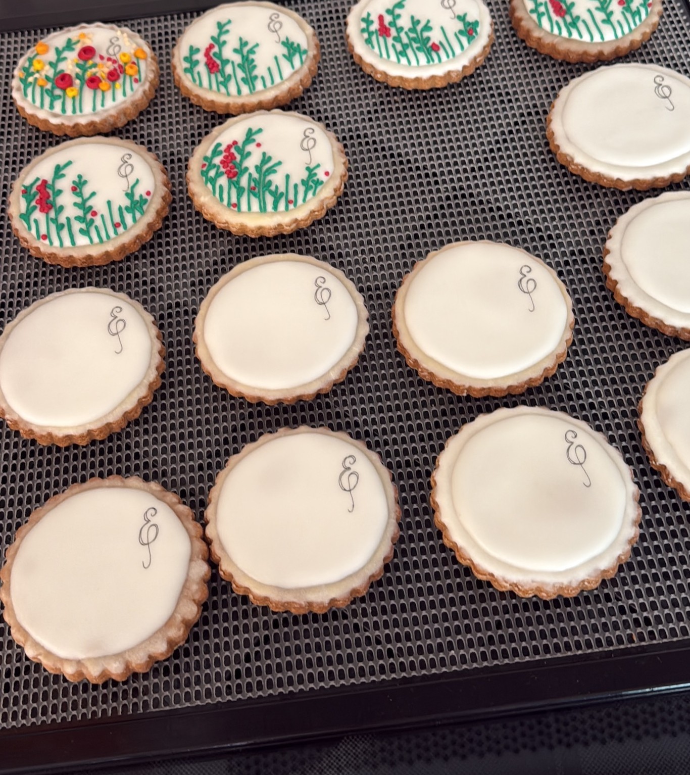 Un grupo de galletas decoradas con royal icing de color blanco, se colocan junto a las galletas de muestra para el diseño final.