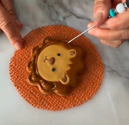En la imagen se muetra una mano decorando una galleta en forma de león con royal icing de color café. Estas galletas decoradas con royal icing son personalizadas para un baby shower.