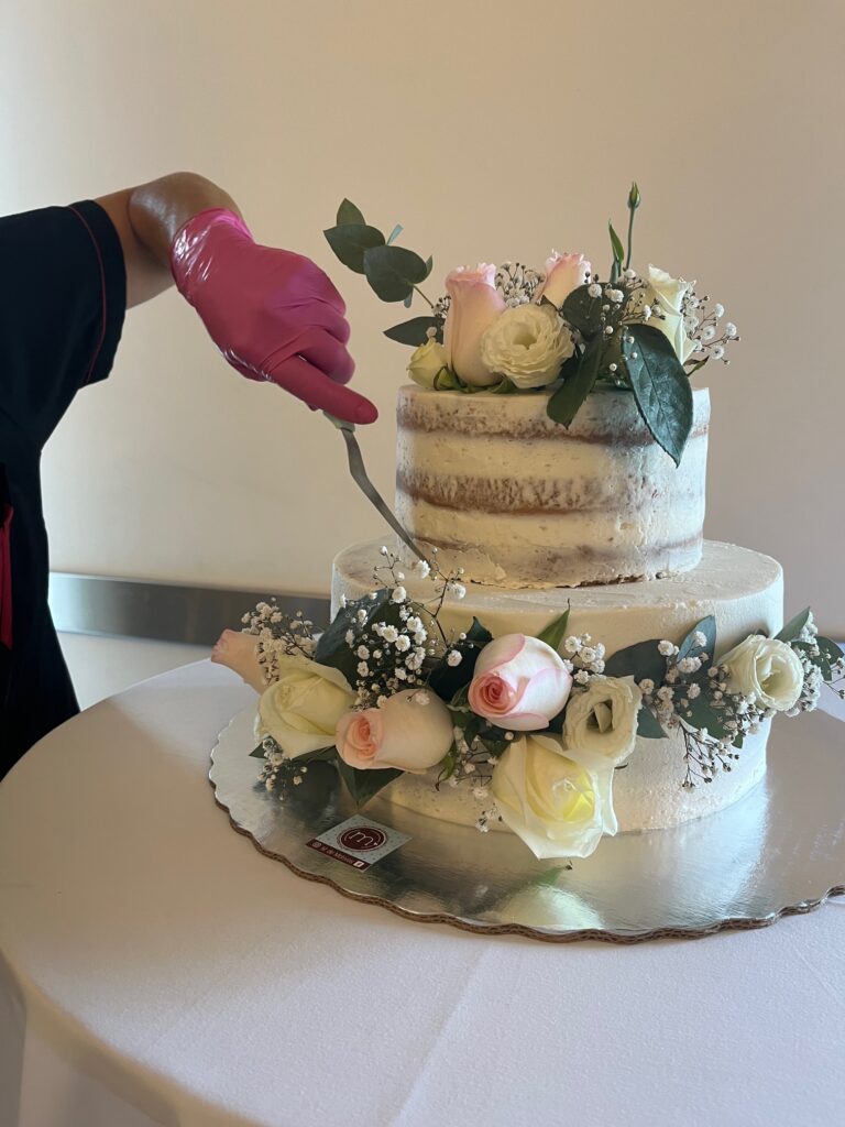 Una mano con un guante rosa decora pastel de boda decorado con rosas. Pasteles personalizados Puebla, m de motivos, hace pasteles personalizados con entrega personal en el lugar del evento.