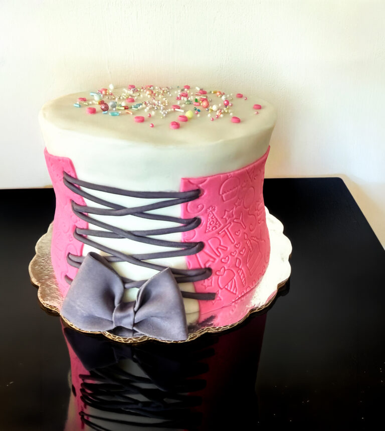 Pasteles fondant para quinceñeras en puebla. Pastel decorado con fondant en forma de corsert color rosa, decorado con sprinkles de colores en la parte superior. El pastel se coloca sobre una base reflectante y sobre una mesa negra.