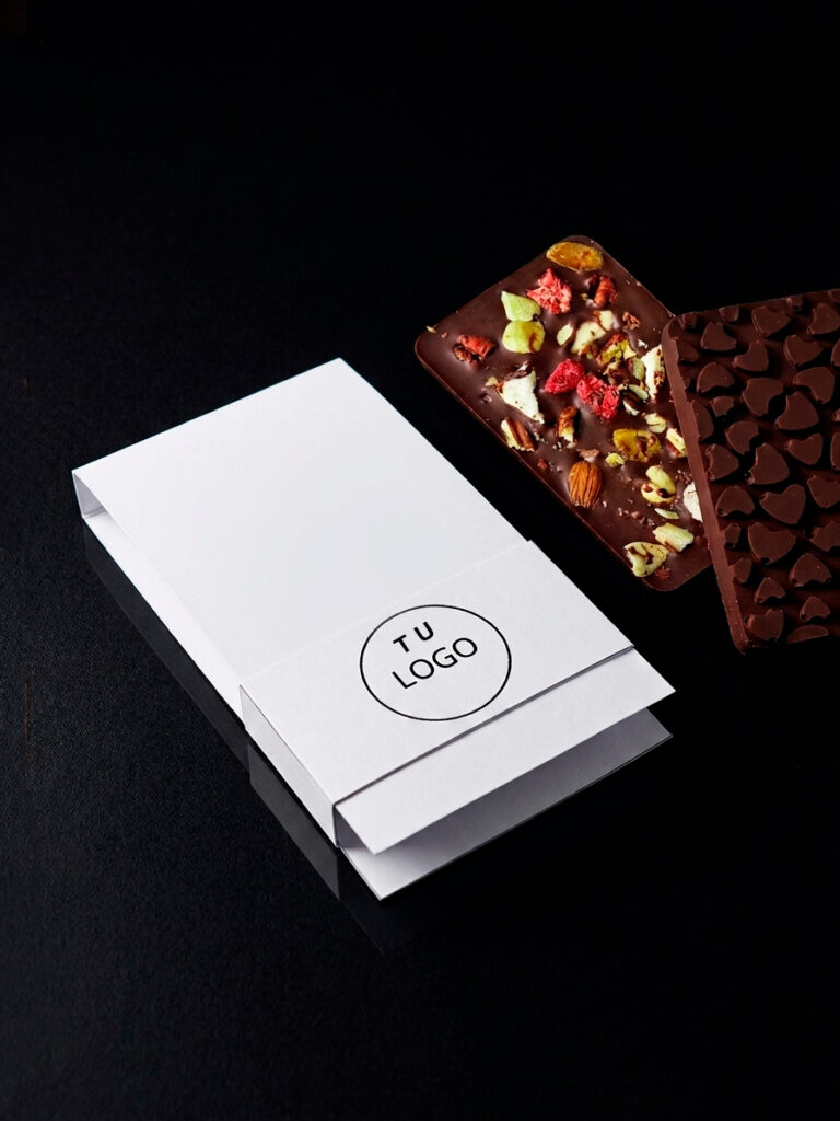 Regalos para clientes personalizados desde el empaque. Barras de chocolate decoradas con frutos secos se colocan junto a una caja blanca con opción para poner logos.